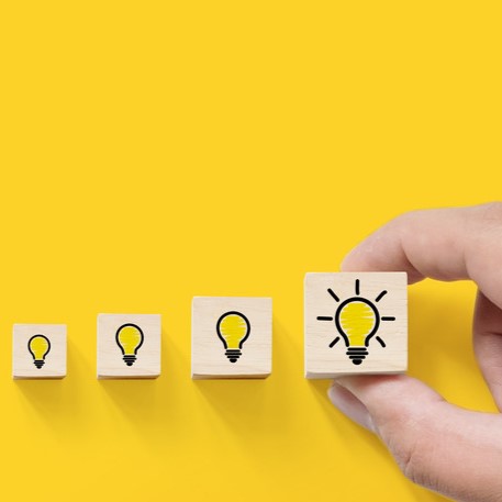 Wooden blocks in a row on a yellow background with lightbulb icons, symbolizing a progression of ideas